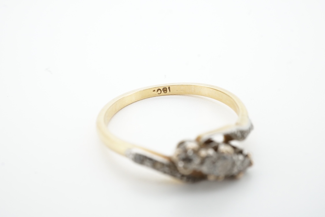 A three-stone diamond ring, early 20th century, centring on a diagonal line of three circular-cut diamonds totalling approximately 0.24 carats, to asymmetrical shoulders set with smaller rose-cut diamonds, mounted in gol